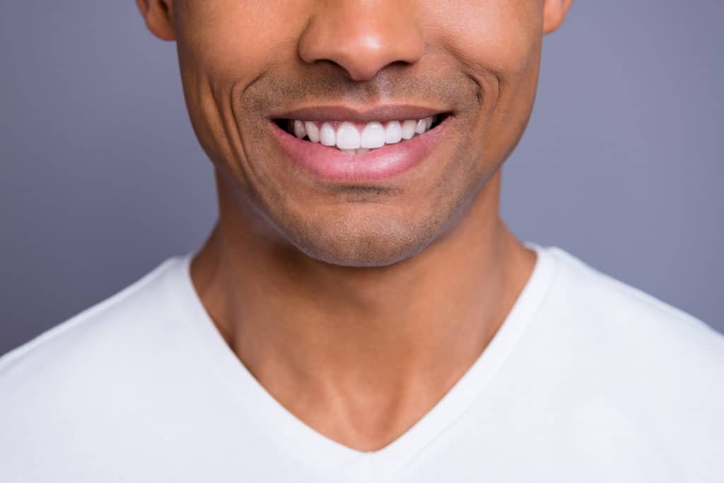 close up of bottom half of man's face smiling with white tee on