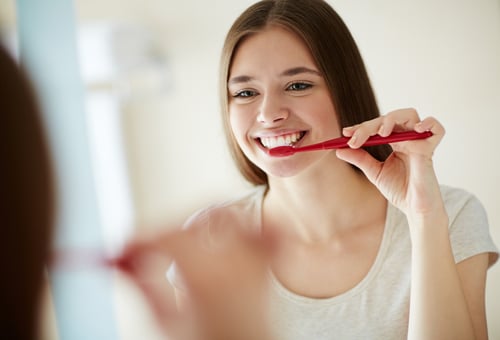 Young woman brushing her teeth at mirror